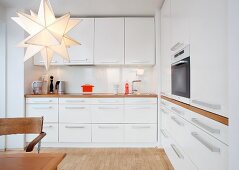 Kitchen with white furnishings, wooden worksurfaces, fitted cooker and star-shaped lamp