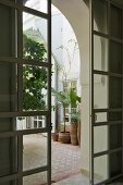 Blick durch geöffnete Schiebetüren in marokkanischen Innenhof mit Topfpflanzen auf Mosaikfliesen