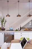 Open-plan interior with kitchen counter below retro pendant lamps & staircase with wooden balustrade