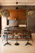 Vintage barstools at counter with glass-fronted drawers in open-plan, fitted kitchen with pendant lamps with lampshades made from stylised leaves; man behind counter