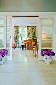 View into interior with sliding, glass 30s' doors flanked by vases of purple hydrangeas on pale wooden floor