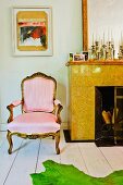 Contemporary artwork above Rococo armchair with pale pink upholstery next to marble fireplace with collection of old candlesticks