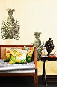 Teilweise sichtbare Sitzbank mit Polster und Kissen neben Tabletttisch an bemalter Wand mit Ananasmotiven