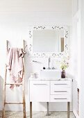 Sink with base cabinet against white tiled wall and below framed mirror next to rustic wooden ladder used as towel rack