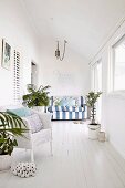 White, maritime-style conservatory with striped sofa, wicker chair and potted plants