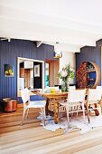 Dining area with animal-skin rug, rustic table and woven chairs in front of blue-painted wooden wall