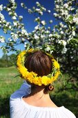 Junge Frau mit Blumenkranz im Haar beim Betrachten eines blühenden Apfelbaums