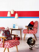 Fifties-style armchairs and side table and vintage floor lamp in front of wall with brightly coloured stripes