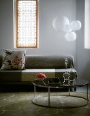 Retro-style, round side table in front of grey sofa and windows with Oriental-style screens flanking spherical pendant lamps