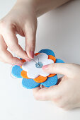 Felt flowers of different sizes and button being sewn together