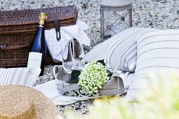 Romantisches Picknick auf Kiesboden mit Kissen, Sekt und Picknickkorb