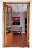 Blick durch offene Tür auf Sitzbank im Rokoko Stil vor Wand mit modernem Bild