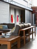 Wooden furniture with grey cushions on terrace of modern, South African beach house; view of beach towels on wall rack through open sliding doors