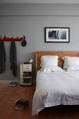 Artistic photo over custom-made bed with wooden headboard in grey-painted bedroom; coat rack to one side