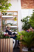 Lesende Frau auf Loftbalkon mit Kräuterregal, Rankgerüst und Blumen in Holztöpfen