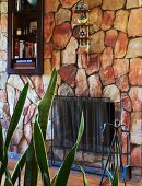 Natursteinwand mit Metallgitter vor der Feuerstelle, Regalnische und Mini-Dekoregal; Sansevieria im Vordergrund