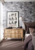 Wallpaper patterned with small black and white architectural pictures in elegant bedroom; framed poster of silhouettes on bedside chest of drawers