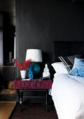 Bed & bedside table with table lamp against black wall