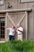 Man and woman talking and gesturing in front of large sliding door in wooden facade in rural surroundings