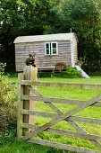 Nostalgic shepherd's hut in meadow on edge of woods; cat sitting on wooden gate