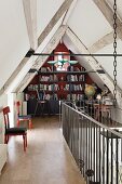 Small library in attic of converted bard with landing balustrade and upholstered wooden chairs