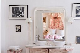 Ensuite bathroom with twin basins on washstand and romantic double bed in country-house style reflected in mirror