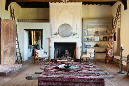 Rustic table with Moroccan tablecloth in spacious, rustic interior with open fireplace in background