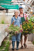 Young woman and mature man walking with hanging baskets in garden centre