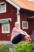 Vergnügte junge Frau auf Holzgeländer sitzend vor rotbraunem Holzhaus