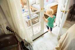 Kleines Mädchen geht durch Tür auf Terrasse; an Ledersessel angelehnte Gitarre im Wohnzimmer