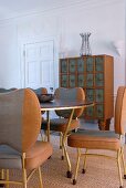 Tubular steel chairs with grey and brown upholstery at dining table; postmodern chest of drawers in background