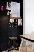 Vintage Hocker und alte Holzplatte auf weissen Tischböcken vor einer schwarz gestrichenen Pinnwand mit Zettelbord und Sternen