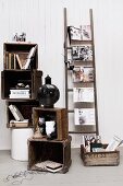 Gestapelte Holzkisten mit Büchern und Deko, daneben eine Leiter mit quergehängten Modezeitschriften