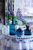 Lupins in blue glass vases on console table with lace trim and gathered fabric below antique mirror