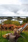 Garden chair with warm fur blankets, cushions and lantern in autumnal garden with view of Norwegian skerry coast