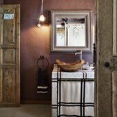 Einblick in ein rustikales Bad - Holzschale als Waschbecken auf gefliestem Waschtisch vor Spiegel an mauvefarbener Wand
