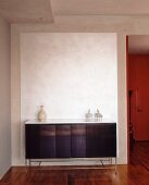 Sideboard with sparse ornaments against white panel on exposed concrete wall
