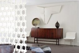 Objets d'art above and on sideboard with dark, exotic wood veneer and white, ornamental partition element in foreground