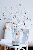 Easter bouquet of white-painted spring branches hung with blown eggs in large glass vase