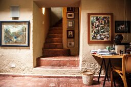 Office with narrow staircase and collection of photographs above desk against rustic wall