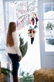 Girl standing in doorway receiving guests arriving on foot through snowy landscape