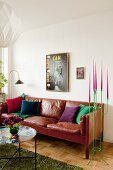 Side table with colourful tray in front of brown leather sofa next to green metal candelabra with pink candles in corner of living room