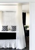 Elegant double bed with black and white textiles and floor-to-ceiling curtains hanging from encircling rod