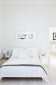 Double bed with white bed linen in minimalist bedroom with open door and view of chairs beyond
