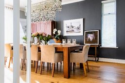Elegantes, anthrazitfarbenes Esszimmer mit langem Esstisch und gepolsterten Armstühlen; über dem Tisch eine verspielte Hängeleuchte aus Meerglas