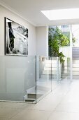 Light-flooded hallway with large skylight, glass balustrade and framed black and white photo on wall with reflections in glass