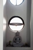 Statue of Buddha below open circular window in niche