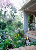 Veranda with brick floor bordered by summer garden and dog jumping up onto veranda