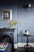 Black fire surround against grey wallpaper; picture with wide silver frame on wall above mantelpiece