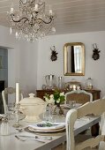 Festively set table in rustic dining room with chandelier hanging from white wooden ceiling